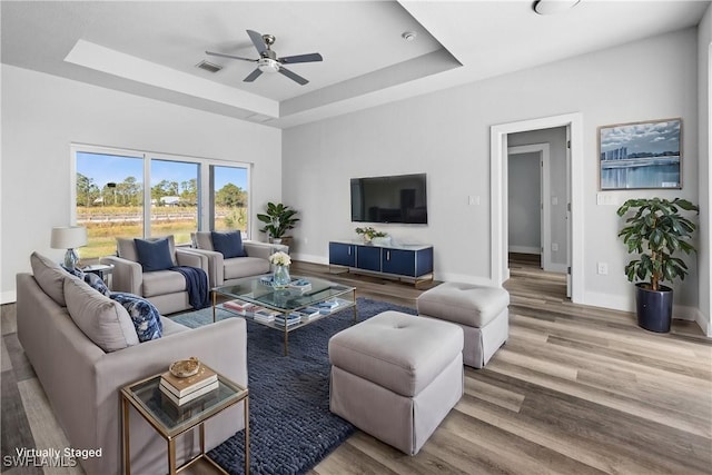 living room with ceiling fan, a raised ceiling, and hardwood / wood-style floors