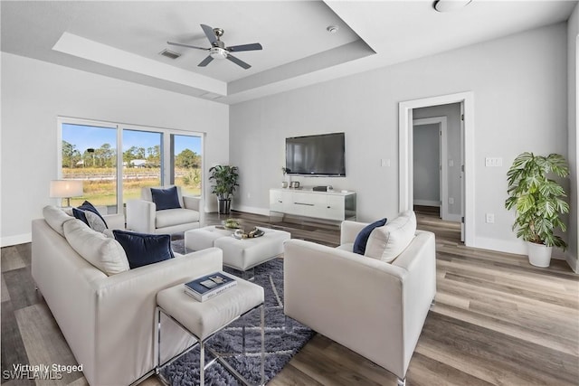 living room featuring hardwood / wood-style flooring, ceiling fan, and a raised ceiling