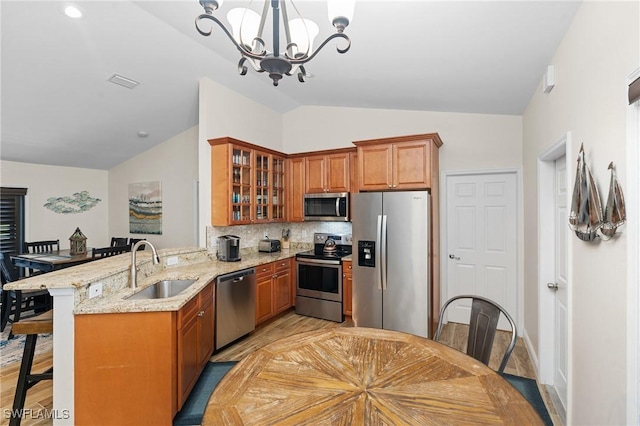 kitchen featuring kitchen peninsula, a chandelier, lofted ceiling, a kitchen bar, and appliances with stainless steel finishes