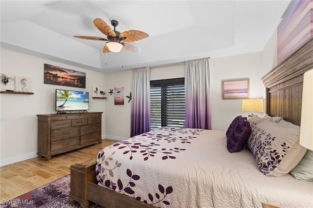 bedroom with a tray ceiling, ceiling fan, and light wood-type flooring