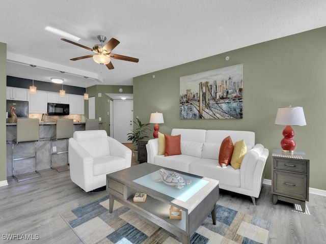 living room featuring ceiling fan, light hardwood / wood-style flooring, sink, and a textured ceiling