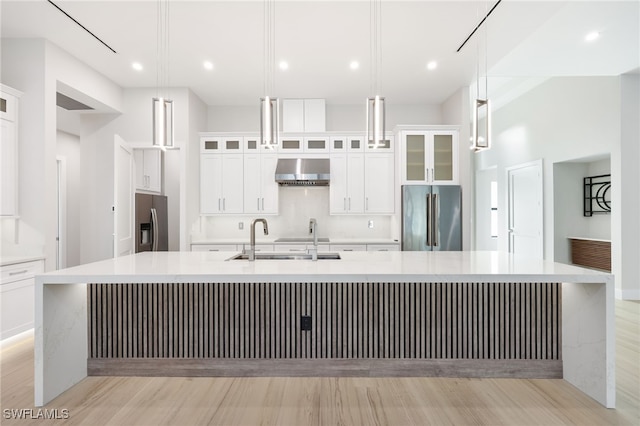 kitchen featuring a large island with sink, stainless steel fridge, hanging light fixtures, and wall chimney range hood