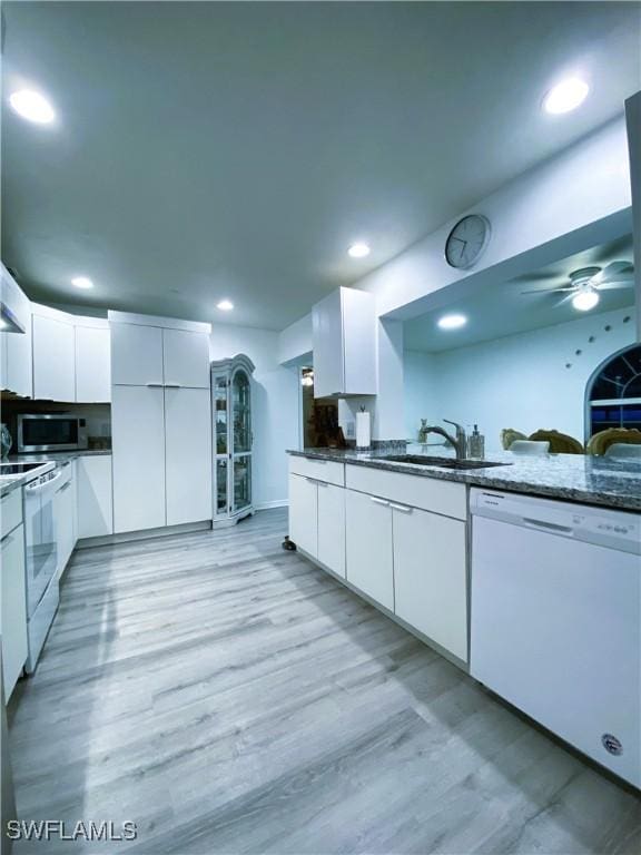 kitchen featuring sink, light hardwood / wood-style flooring, white appliances, dark stone counters, and white cabinets