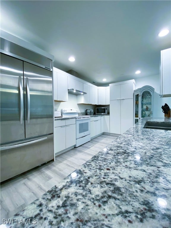 kitchen with light wood-type flooring, under cabinet range hood, white cabinetry, stainless steel appliances, and stone counters