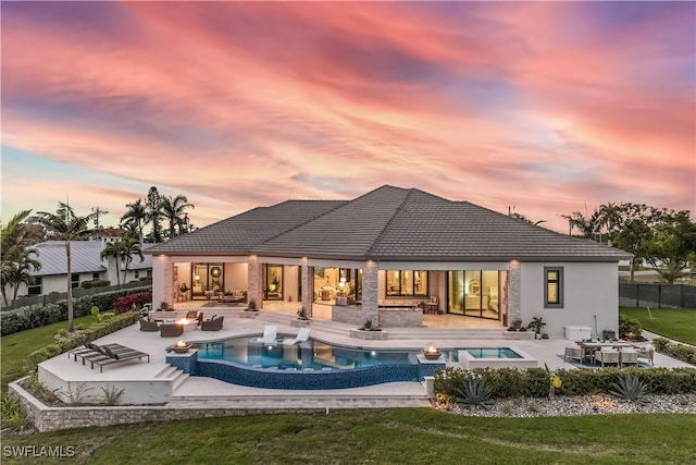 back house at dusk featuring area for grilling, an outdoor living space with a fire pit, a pool with hot tub, a patio area, and a yard