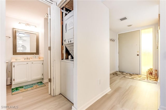 hallway featuring light hardwood / wood-style floors, sink, and stacked washer / dryer