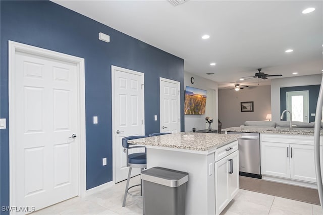 kitchen with light stone countertops, white cabinetry, a center island, ceiling fan, and stainless steel dishwasher