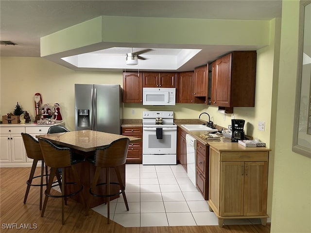 kitchen featuring sink, a tray ceiling, light hardwood / wood-style floors, white appliances, and a breakfast bar area