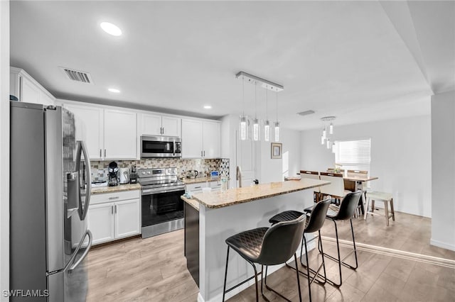 kitchen with light stone countertops, stainless steel appliances, decorative light fixtures, white cabinets, and a kitchen island