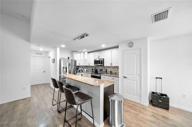 kitchen with a kitchen island with sink, white cabinets, stainless steel appliances, and light wood-type flooring