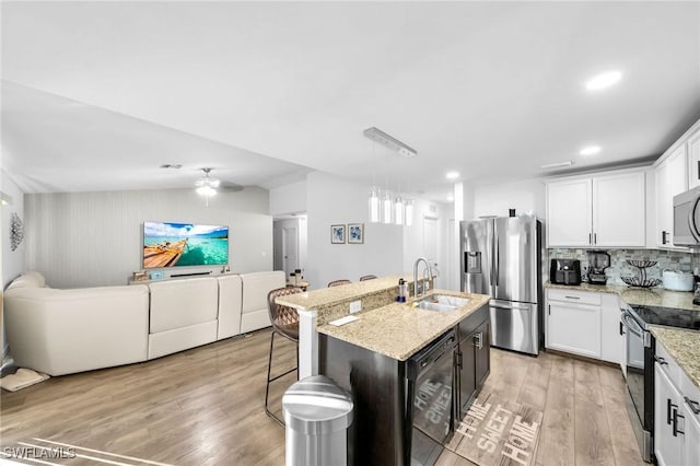 kitchen with pendant lighting, a kitchen island with sink, white cabinets, sink, and appliances with stainless steel finishes