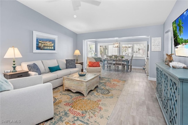 living room with ceiling fan, light hardwood / wood-style floors, and vaulted ceiling