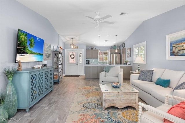 living room with ceiling fan, vaulted ceiling, and light wood-type flooring