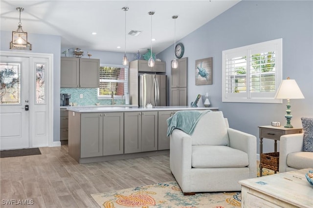 kitchen featuring gray cabinetry, light hardwood / wood-style floors, stainless steel refrigerator, hanging light fixtures, and lofted ceiling