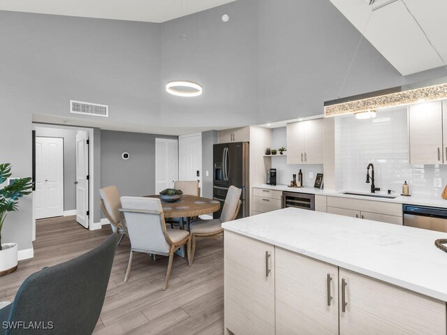 kitchen with sink, wine cooler, light hardwood / wood-style flooring, decorative backsplash, and appliances with stainless steel finishes