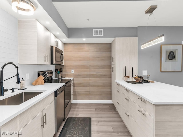 kitchen with sink, light hardwood / wood-style floors, decorative light fixtures, and appliances with stainless steel finishes