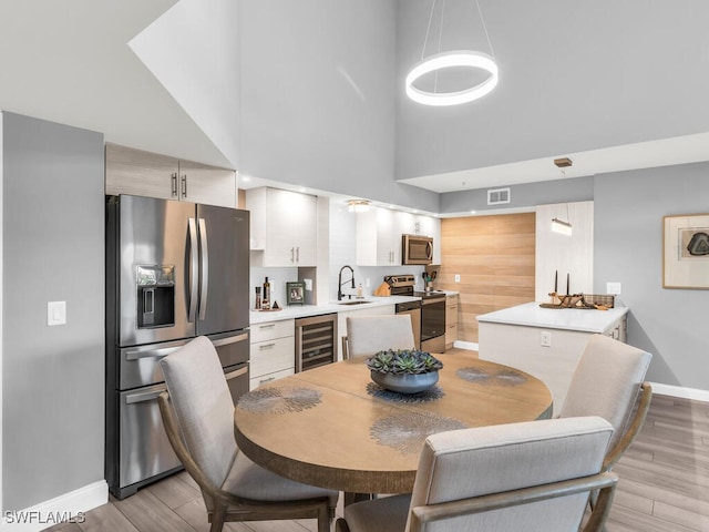 dining area featuring a high ceiling, light hardwood / wood-style flooring, wine cooler, and sink