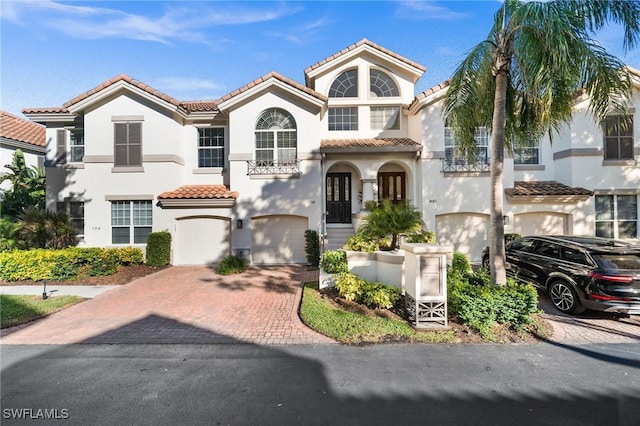 mediterranean / spanish house featuring a garage, a tiled roof, decorative driveway, and stucco siding