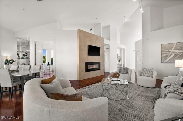 living room featuring a tiled fireplace, dark wood-type flooring, and high vaulted ceiling