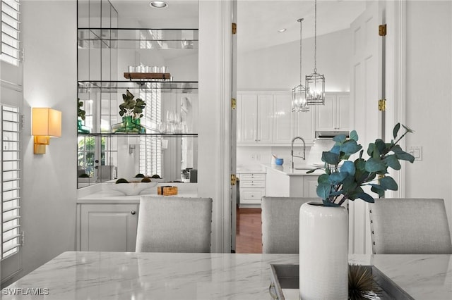 bar featuring a towering ceiling, wood finished floors, a sink, and decorative light fixtures