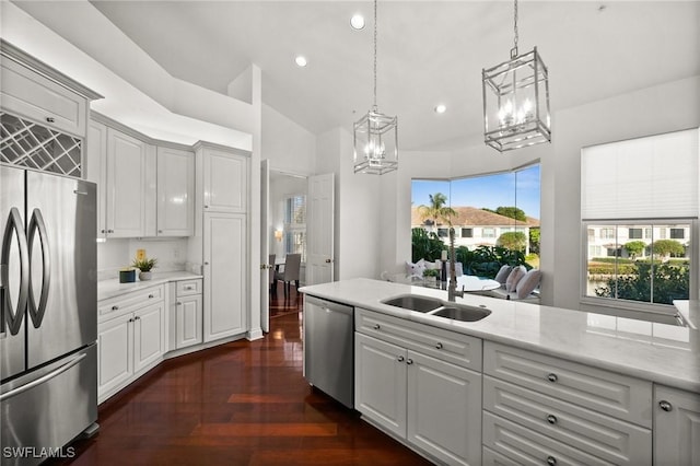 kitchen featuring sink, appliances with stainless steel finishes, hanging light fixtures, light stone counters, and vaulted ceiling