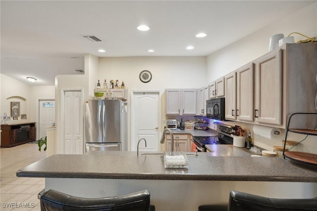 kitchen with a breakfast bar, sink, light tile patterned floors, appliances with stainless steel finishes, and kitchen peninsula