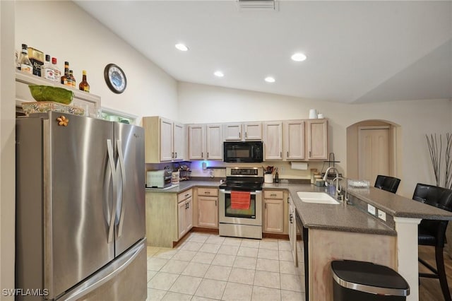 kitchen with sink, lofted ceiling, a kitchen bar, light brown cabinetry, and black appliances