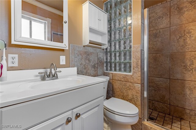 bathroom featuring crown molding, toilet, a shower with door, vanity, and tile walls