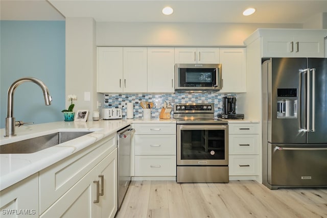 kitchen with light stone countertops, white cabinetry, sink, stainless steel appliances, and light hardwood / wood-style flooring