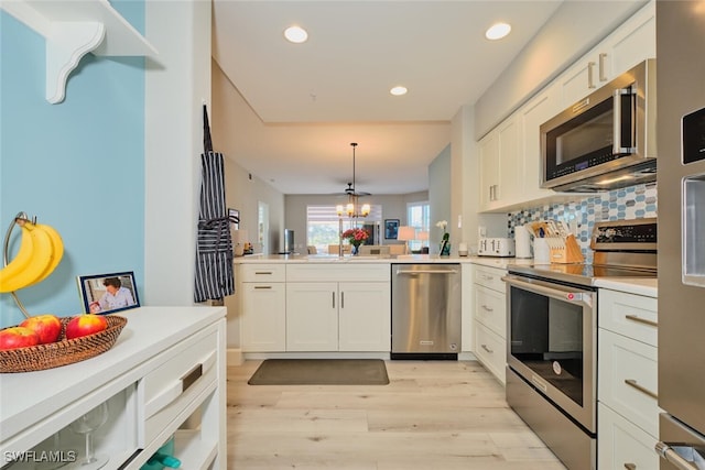 kitchen with kitchen peninsula, appliances with stainless steel finishes, pendant lighting, white cabinets, and light wood-type flooring