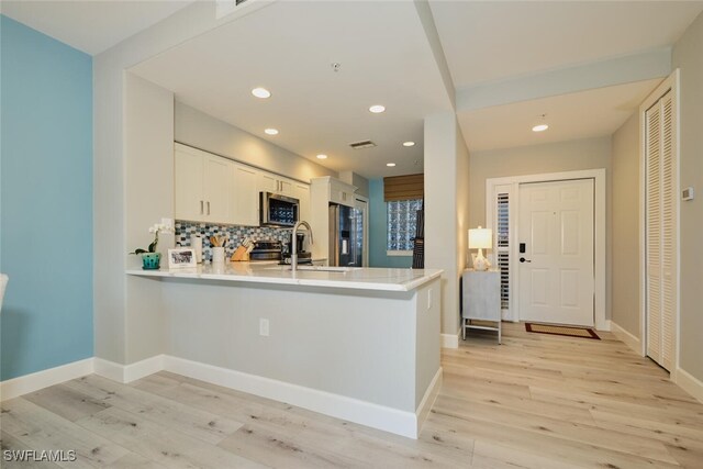 kitchen with white cabinets, kitchen peninsula, appliances with stainless steel finishes, and light hardwood / wood-style flooring