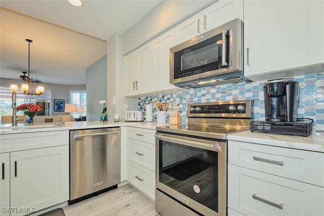 kitchen featuring appliances with stainless steel finishes, light wood-type flooring, tasteful backsplash, white cabinets, and a chandelier