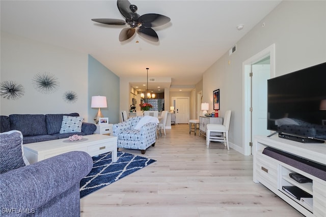 living room featuring ceiling fan with notable chandelier and light wood-type flooring