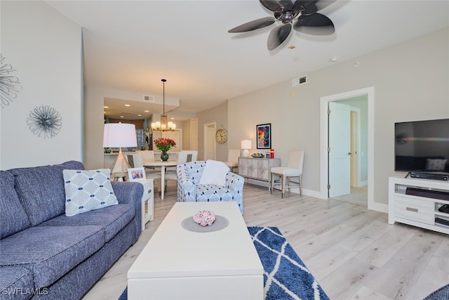 living room featuring ceiling fan with notable chandelier and light wood-type flooring