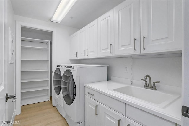 laundry room with cabinets, light wood-type flooring, washing machine and dryer, and sink