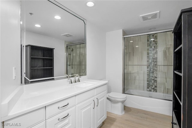 full bathroom featuring shower / bath combination with glass door, hardwood / wood-style floors, vanity, and toilet