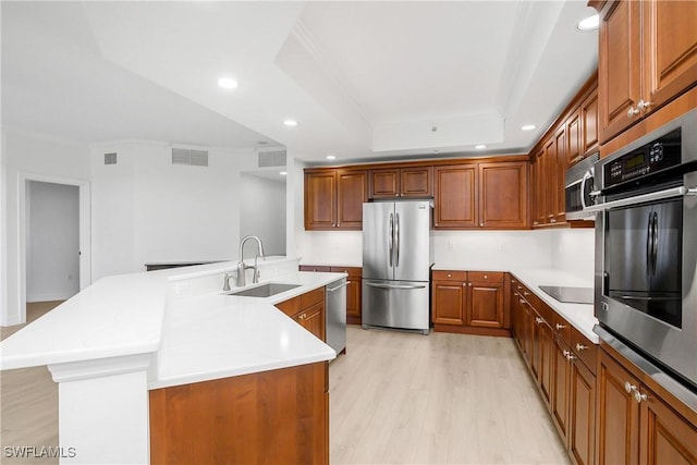 kitchen with stainless steel appliances, a tray ceiling, sink, a center island with sink, and light hardwood / wood-style flooring