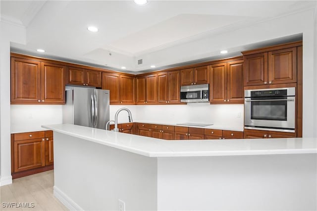 kitchen featuring a center island with sink, crown molding, appliances with stainless steel finishes, a tray ceiling, and light hardwood / wood-style floors