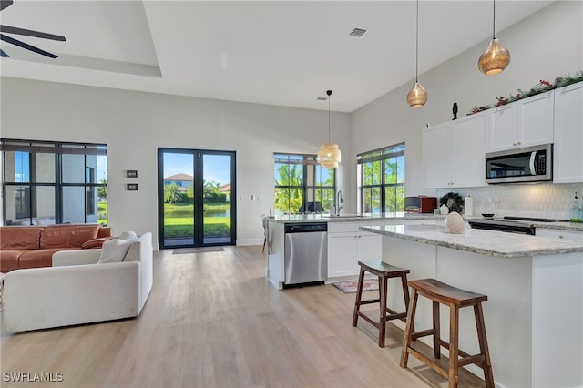 kitchen with plenty of natural light, white cabinets, hanging light fixtures, and appliances with stainless steel finishes