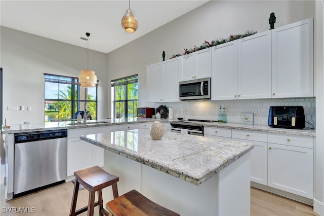 kitchen with white cabinetry, light hardwood / wood-style floors, decorative light fixtures, and appliances with stainless steel finishes