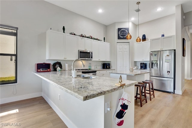 kitchen featuring pendant lighting, kitchen peninsula, appliances with stainless steel finishes, white cabinetry, and a breakfast bar area