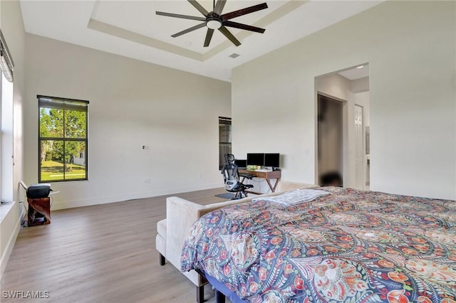 bedroom with ceiling fan, light hardwood / wood-style floors, and a tray ceiling