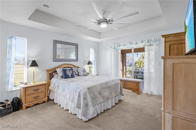 carpeted bedroom featuring ceiling fan, a raised ceiling, and multiple windows