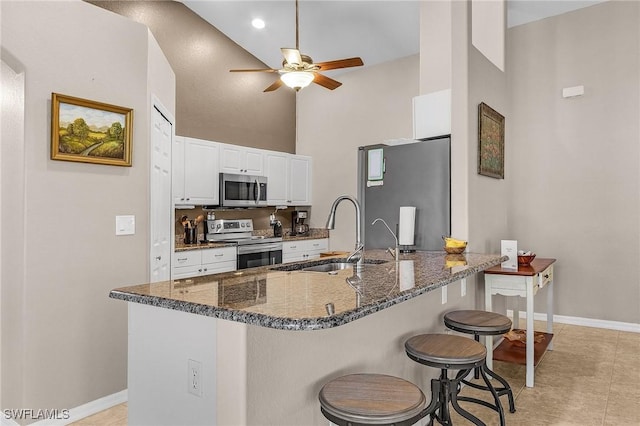 kitchen with a high ceiling, sink, appliances with stainless steel finishes, white cabinetry, and a breakfast bar area