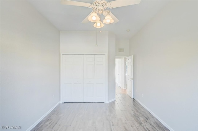 unfurnished bedroom featuring a towering ceiling, light wood-type flooring, a closet, and ceiling fan