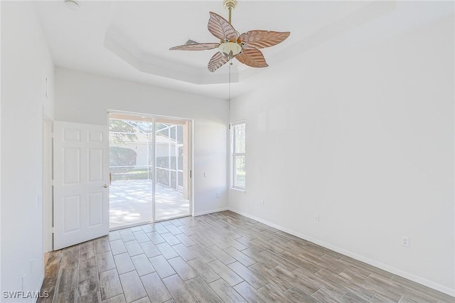 empty room with light wood-type flooring, a raised ceiling, and ceiling fan