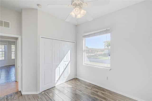 unfurnished bedroom featuring multiple windows, ceiling fan, a closet, and light wood-type flooring