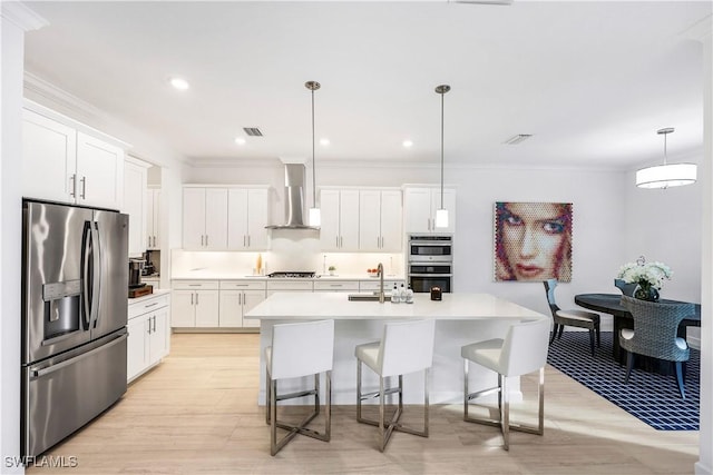 kitchen featuring wall chimney exhaust hood, white cabinetry, stainless steel appliances, and hanging light fixtures