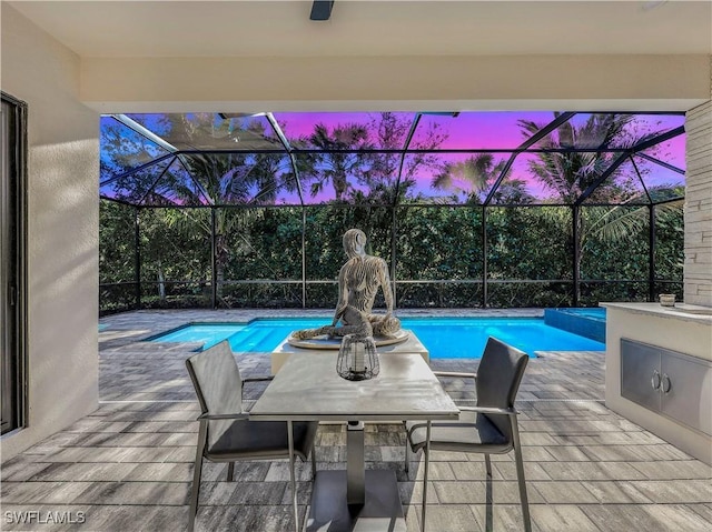 pool at dusk with glass enclosure and a patio