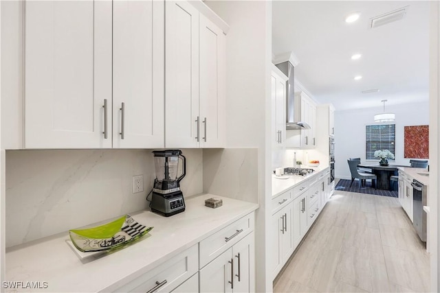 kitchen with white cabinets, appliances with stainless steel finishes, pendant lighting, and wall chimney exhaust hood